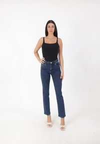 Bodysuit sans manches noir associé à un jean taille haute bleu, présentant une coupe droite et un léger effet usé, complété par des sandales à talons transparents.