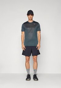 Nike atletische outfit met een donkergroen T-shirt met korte mouwen en zwarte korte broek. Inclusief een zwarte pet en grijze sokken met zwarte accenten.