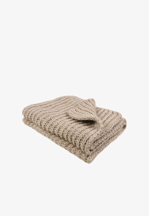 Couverture en tricot beige avec un motif texturé, présentant un coin replié révélant un bord lisse. Fabriquée en fil doux et épais.
