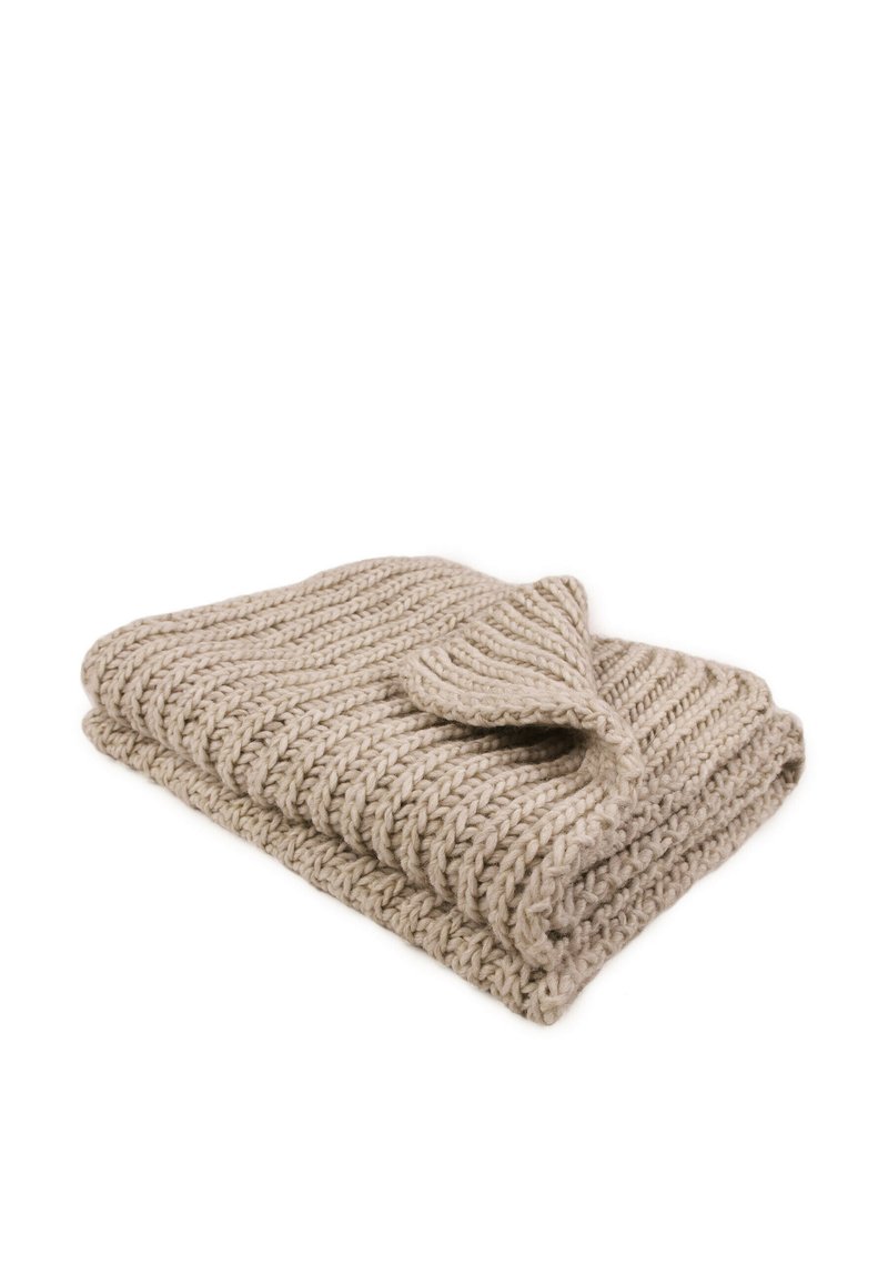 Gehaakte deken in beige met een gestructureerd patroon, met een omgevouwen hoek die een gladde rand onthult. Gemaakt van zacht, chunky garen.