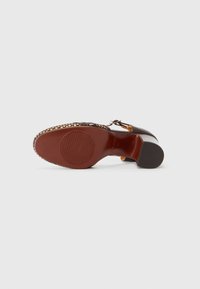 Sole di scarpa in pelle marrone con un design testurizzato. Presenta una punta arrotondata, un tacco leggermente elevato e decorazioni lungo il bordo.