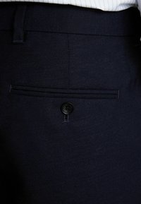 Pantalons taillés bleu marine en tissu texturé. Dotés d'une poche arrière simple avec un bouton noir et d'une taille plate.