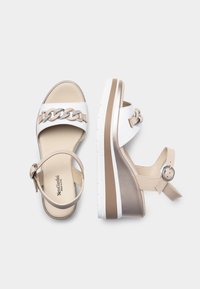Beige and white high-heeled sandals featuring a chain accent, ankle strap, and a textured rubber outsole with a metallic sheen on the heel.