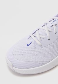 Violeta un balts sporta apavi ar teksturētu tīkla augšdaļu, kontrastējošu zilu logotipu un baltu gumijas zoli ar rakstainu protektoru.