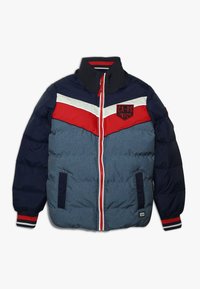 Chaqueta acolchada para niño con mangas en color marino, cuerpo azul, franja en chevrón rojo y blanco en el pecho, cremallera roja y parche en el lado superior izquierdo.
