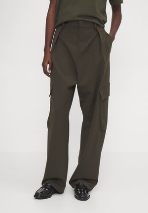 Olivgrüne Cargo-Hosen mit weitem Bein, gefaltetem Vorderteil, seitlichen Taschen und glatter Textur, kombiniert mit schwarzen Slippers.