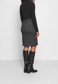 Zwarte blouse met lange mouwen, gecombineerd met een knie-lange, gestructureerde, zwart-wit gestreepte kokerrok en knie-hoge zwarte leren laarzen.