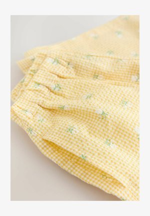 Geel ruitstof met kleine witte bloemenpatronen. Kenmerkt zich door geplooide details en een zachte textuur, ideaal voor lichtgewicht kleding.