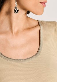 Beige geripptes Oberteil mit rundem Halsausschnitt und metallic Akzenten, kombiniert mit silbernen blumenförmigen Ohrringen. Glatte Textur mit subtiler glänzender Oberfläche.