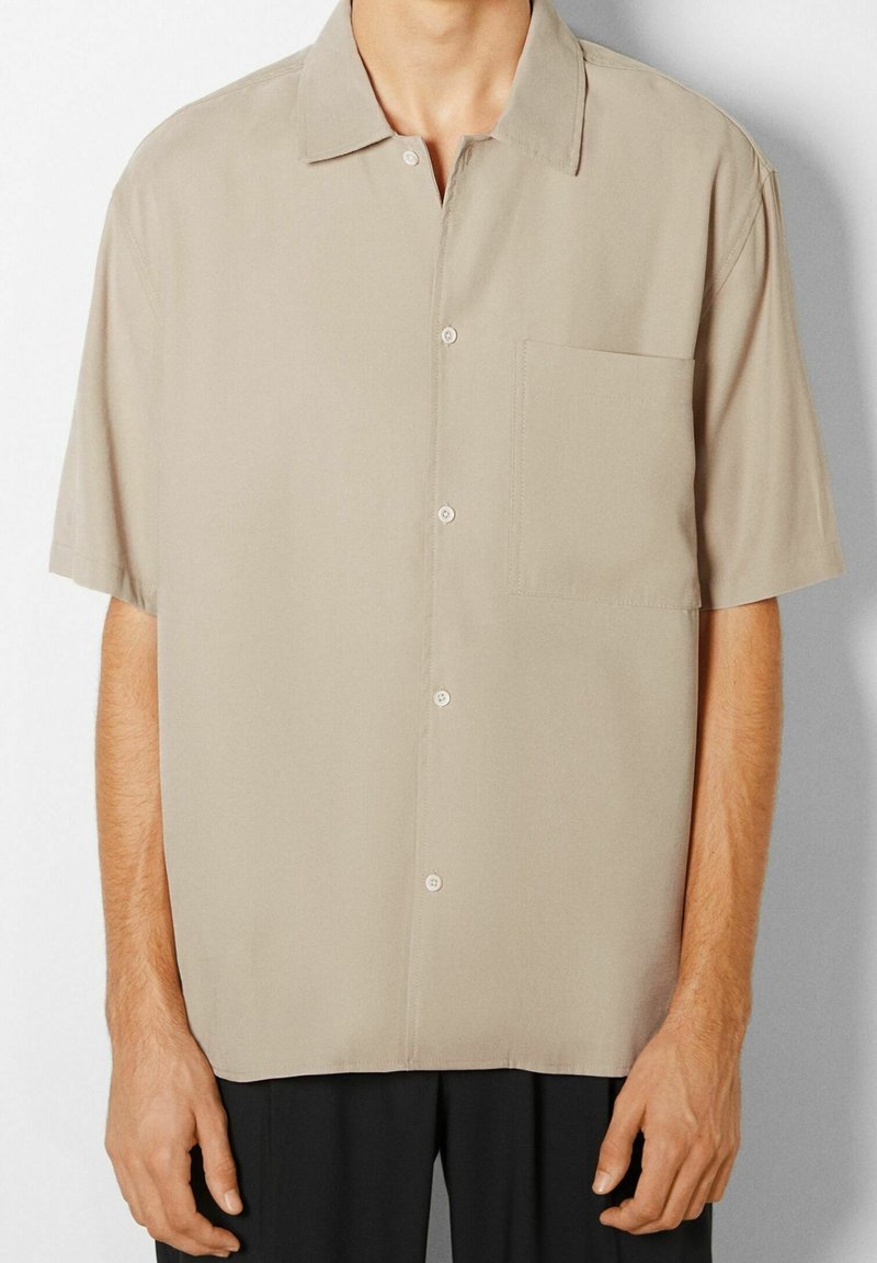Short-sleeve button-up shirt in a light beige fabric. Notable features include a chest pocket, soft texture, and a classic collar design.