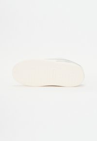 Fehér sneaker talp, textúrált mintával, sima felső peremmel és minimális bézs és szürke díszítéssel.
