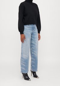 Czarny dziergany sweter z golfem, jasnoniebieskie dżinsy o szerokich nogawkach z lekkim przetarciem i błyszczącymi detalami oraz czarne szpilki z ostrym noskiem i metalicznymi zakończeniami.