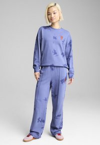 Violetā tievā auduma džemperis ar saskaņotām sporta biksēm, ar izšūtu dizainu uz krūtīm un sāniem. Mīksts audums ar brīvu piegriezumu.