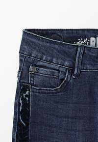 Jeans de denim de color azul oscuro, con una tela texturizada, un pequeño bolsillo frontal y un acento negro brillante a lo largo del costado.