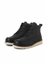 Botas de cuero negras hasta el tobillo con suelas de goma beige, con punta redondeada, diseño de cordones y detalles de costura en contraste.