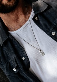 Silverhänge i kedja över en strukturerad vit T-shirt, lager på lager med en mörk skjorta.