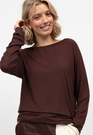 Brązowa bluzka z długim rękawem, dekoltem w łódkę i luźnym krojem. Miękka tkanina o gładkiej fakturze. Połączona z jasnymi, wzorzystymi spodniami.