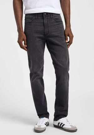 Mörkgrå denimjeans med slim fit, med fem fickor, dragkedja och en enkel metallknapp som stängning. Bärs med vita och grå sneakers.