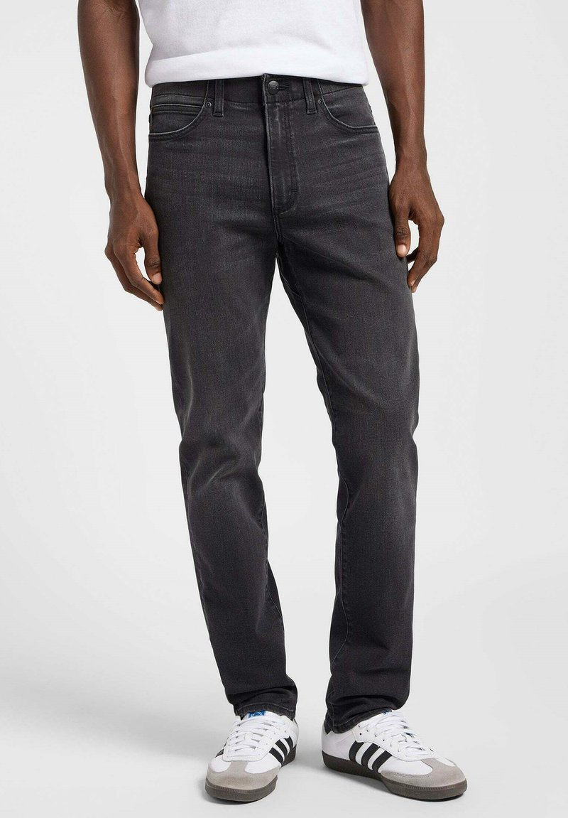 Jeans de mezclilla gris oscuro con un corte ajustado, que cuentan con cinco bolsillos, una cremallera y un cierre de botón metálico básico. Combinados con zapatillas blancas y grises.