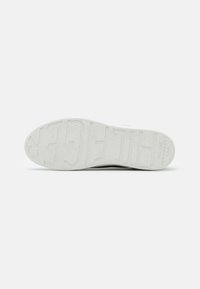 Semelle de basket blanche avec grand marquage en relief « HILFIGER » et petit texte « EST. 1985 NEW YORK CITY U.S.A. » au talon.