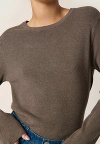 Brauner gerippter Strickpullover mit Rundhalsausschnitt und langen Ärmeln, kombiniert mit hochtaillierten Jeans. Weicher Stoff, figurbetontes Design.