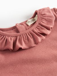 Top in cotone rosa a coste con colletto volant e chiusura a bottoni sul retro. Etichetta con "Maiami Copenhagen" visibile.