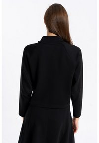 Czarna krótka kurtka z stojącym kołnierzem i rękawami do trzech czwartej. Gładki materiał z delikatnymi detalami szycia. Prosty design, bez wzorów.