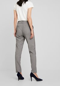 Szare spodnie w kratę o dopasowanym kroju, z średnim stanem i bocznymi kieszeniami, zestawione z czarnymi szpilkami.