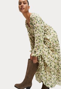 Blumiges Maxikleid in Grün und Creme mit Puffärmeln, kombiniert mit knielangen braunen Wildlederstiefeln mit Blockabsatz.