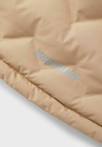 Veste matelassée beige avec une texture lisse et brillante. Dotée d'un logo argenté réfléchissant et de coutures horizontales le long de l'ourlet.