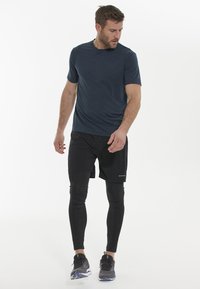 Marinblus kortärmad sporttröja i kombination med svarta knälånga shorts och svarta leggings. Sneakers har grå och blå detaljer.
