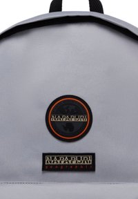 Zaino grigio realizzato in tessuto testurizzato, con un logo ricamato rotondo nero e arancione e un'etichetta rettangolare nella parte inferiore.