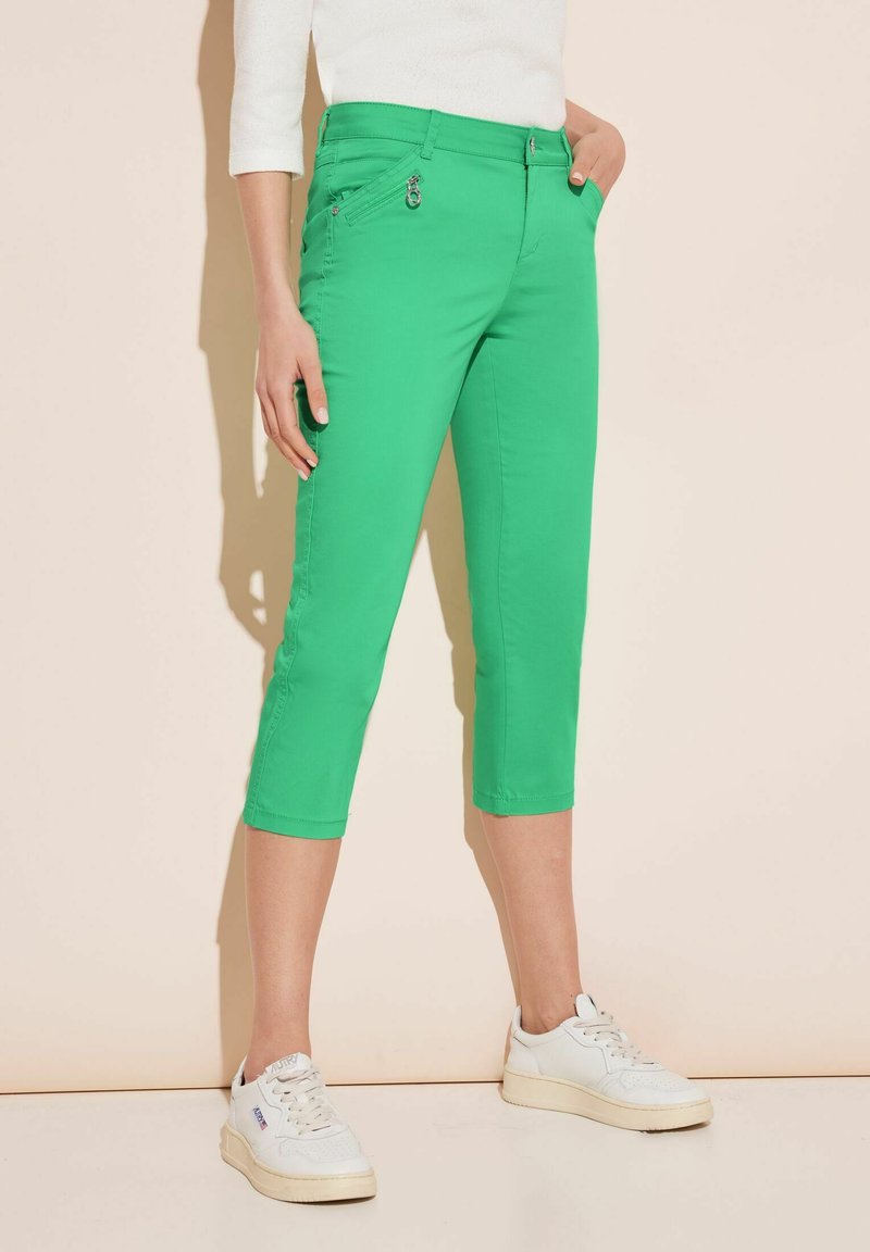 Pantaloni capri verdi in cotone misto, dotati di una tasca frontale con zip, vestibilità slim e orli rifiniti. Indossati con sneakers bianche.