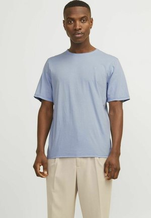 Light blue cotton t-shirt with short sleeves, round neckline, subtle logo on the chest, paired with light beige trousers.