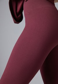 Leggings ribbi burgundii cu talie înaltă, textură netedă și design ajustat, punând în evidență forma picioarelor.