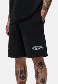Zwarte shorts van katoen met een rechte pasvorm, voorzien van witte geborduurde branding op de linkerzoom en een zachte textuur.