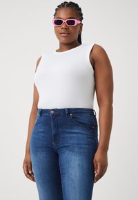 Λευκή αμάνικη μπλούζα, μπλε τζιν με ελαφριά ξεθώριασμα και ροζ ορθογώνια γυαλιά ηλίου. Το ντύσιμο διαθέτει έναν απλό, casual σχεδιασμό και καθαρές γραμμές.