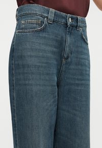 Τζιν παντελόνια σε σκούρο μπλε με ευθεία γραμμή ποδιού. Περιλαμβάνουν ζώνη με κουμπί, μπροστινή τσέπη και ξεθωριασμένη υφή.