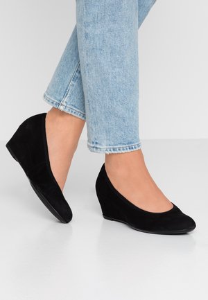 Chaussures compensées en suede noir avec un bout rond et un talon compensé bas, associées à un jean cropped bleu clair. Texture lisse, design minimaliste.