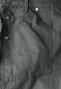 Mörkgröna bomullsshorts med en stor bakficka som har metallknappar och synliga söm detaljer. Slät, rynkig textur.