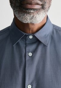Camisa de patrón naval con cuello, que presenta una tapeta con tres botones de color claro y una tela texturizada.