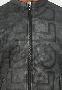 Chaquetón negro fabricado en material texturizado con un sutil acabado mate, que presenta un cierre central y un patrón de logo emblema prominente.