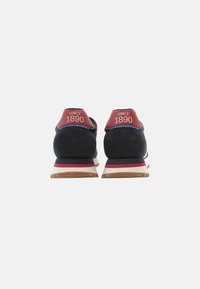 Zapatillas de deporte en azul marino y rojo con una parte superior texturizada, que cuentan con una entresuela blanca y una suela de goma. "DESDE 1890" impreso en la etiqueta del talón rojo.