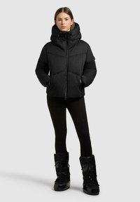 Sort pufferjakke med høj krave, lynlås og sidelommer. Bæres med sorte leggings og høje, strukturerede sorte støvler.