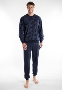 Navy blue loungewear set with long-sleeve top featuring a pocket and geometric pattern, paired with matching tapered pants. Soft fabric.
