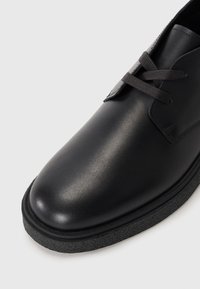 Zwarte leren schoen met een gladde afwerking, ronde neus en grijze veters. Beschikt over een getextureerde rubberen zool voor grip en duurzaamheid.