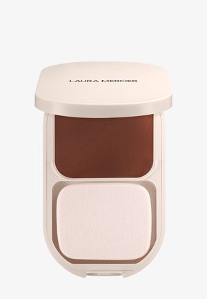 Poudre compacte avec un boîtier de couleur crème, présentant une section de poudre bronzante au-dessus et un applicateur blanc en dessous. Texture lisse et design épuré.