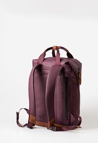 Zaino viola con tessuto liscio, spallacci imbottiti, maniglie superiori e una tasca con zip laterale. Accentato in pelle sulla maniglia superiore.
