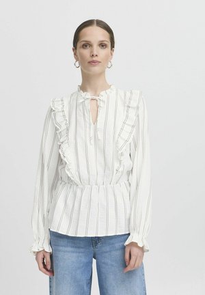 Blusa bianca con righe verticali, dettagli a balze sul collo e sui polsini, apertura a chiave e vita arricciata. Indossata con denim.