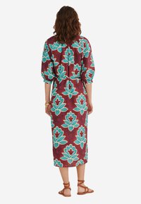 Maroone midi kjole med turkise blomsterprint, korte pufærmer og taljebind. Båret med brune sandaler med stropper.
